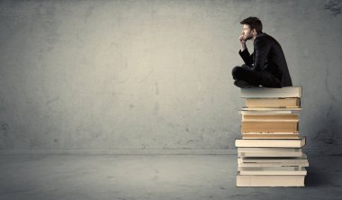 Öğrenci kitap yığınının üzerinde oturuyor
