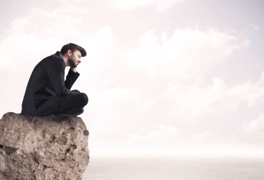 İş adamı taşın üstünde oturuyor.