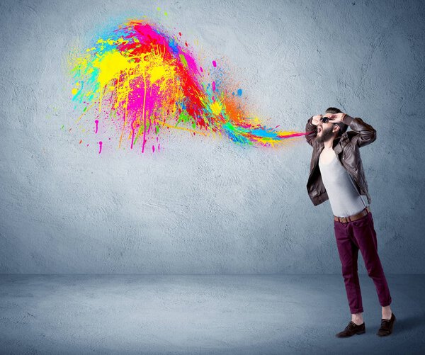 Hipster guy shouting colorful paint on wall