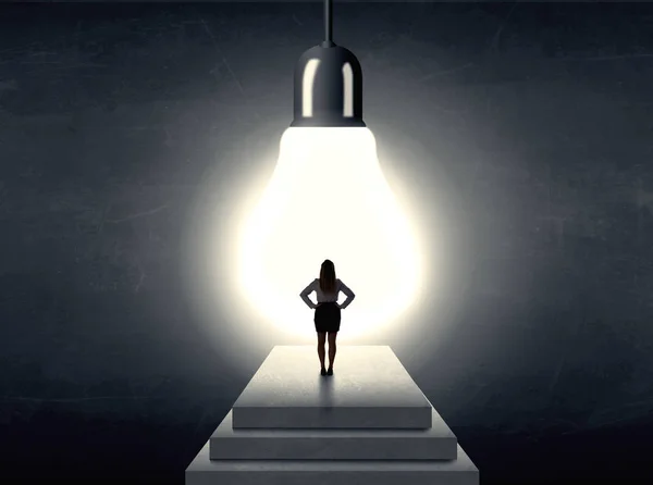 Woman standing on a step in front of a huge light bulb — Stock Photo, Image