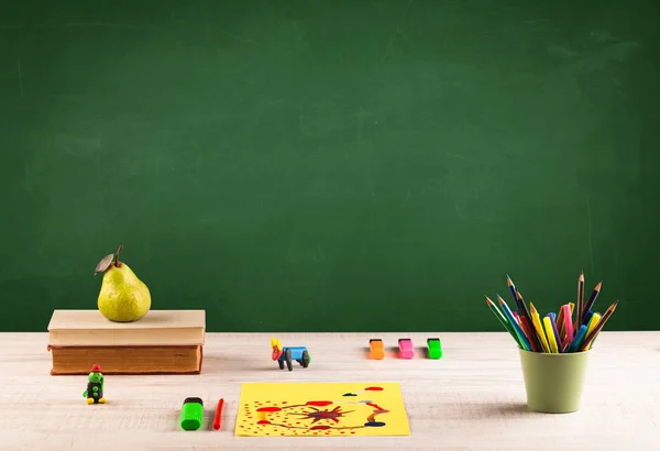 Itens escolares na mesa com quadro-negro vazio — Fotografia de Stock