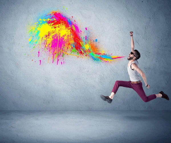 Hipster guy shouting colorful paint on wall — Stock Photo, Image