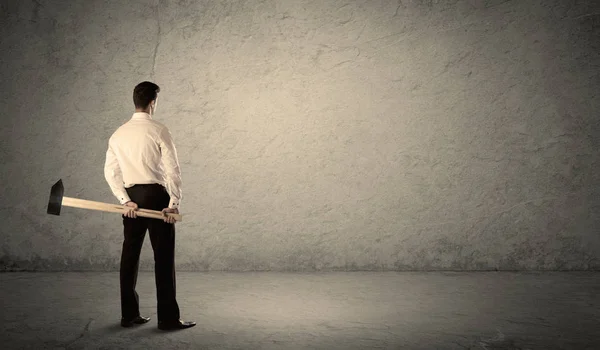 Hombre de negocios de pie frente a una pared grumosa con un martillo — Foto de Stock