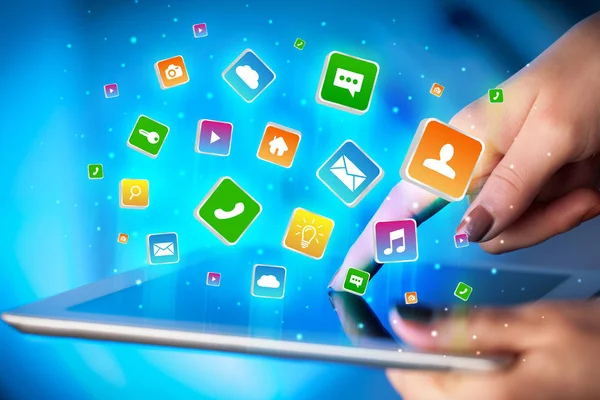Hand using tablet with application icons flying around — Stock Photo, Image