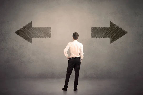 Business man taking a decision while standing in front of two grungy arrows on wall — Stock Photo, Image