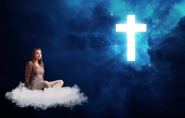 Femme assise sur un nuage regardant une croix — Photo