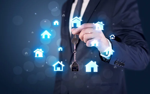 Businessman holding keys with houses around — Stock Photo, Image