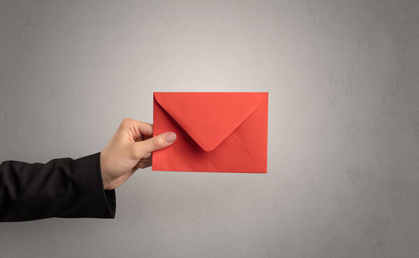 Hand holding envelope with empty wall background