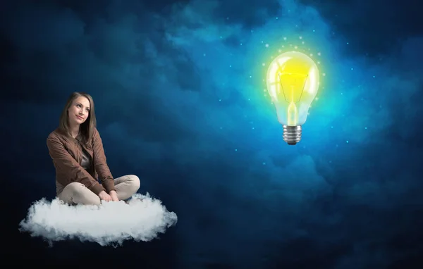 Woman sitting on a cloud lokking at huge lightbulb — Stock Photo, Image