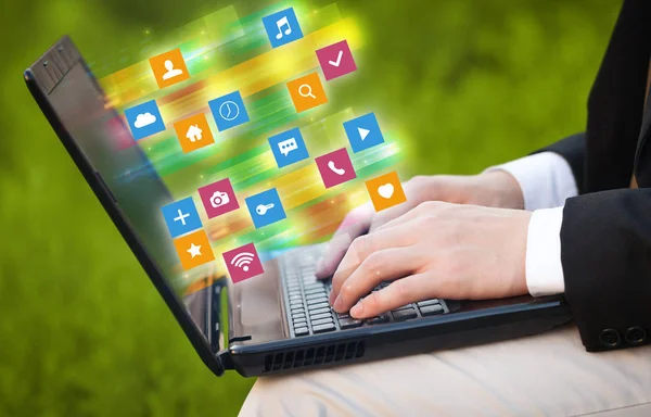 Hand mit Laptop mit bunten Anwendungssymbolen und Symbolen Konzept — Stockfoto
