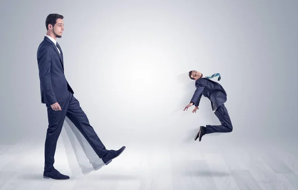 Giant businessman kicking out little businessman