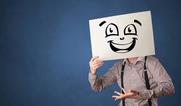 Person holding a paper in front of his face with doodle emoticon — Stock Photo, Image