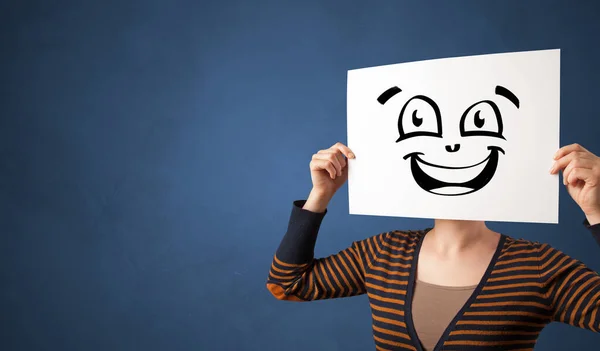 Persona sosteniendo un papel delante de su cara con emoticono garabato — Foto de Stock