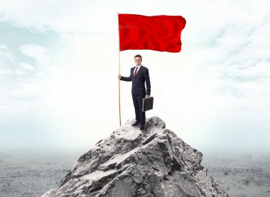 Businessman on the top of a the mountain holding flag clipart