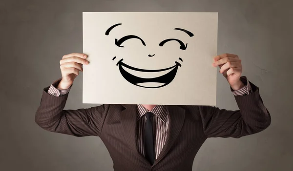 Person holding a paper in front of his face with doodle emoticon — Stock Photo, Image