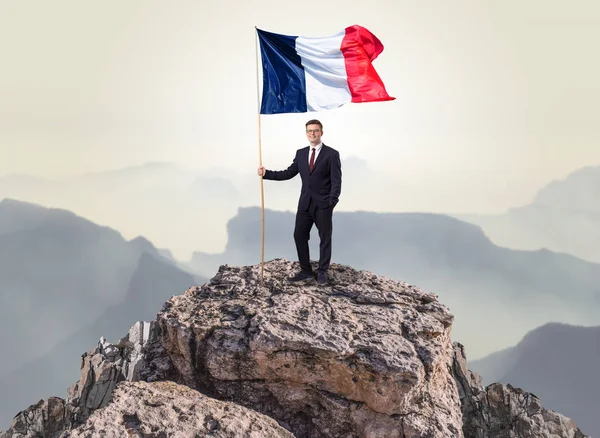 Бизнесмен на вершине скалы с флагом — стоковое фото