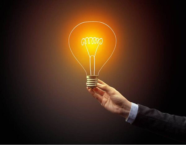 рука держа лампочку на темном фоне