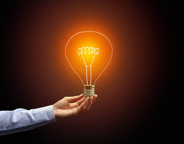 рука держа лампочку на темном фоне