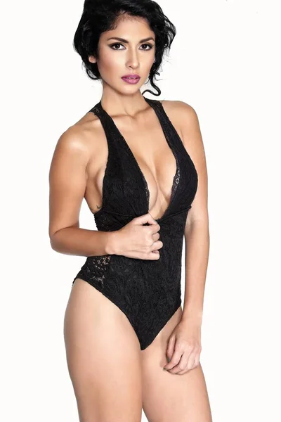 Çok seksi dövmeleri olan, siyah bir iç çamaşırı giyen, kendine güvenen ve baştan çıkarıcı bir tavırla ayakta duran genç bir kadının şehvetli görüntüsü.