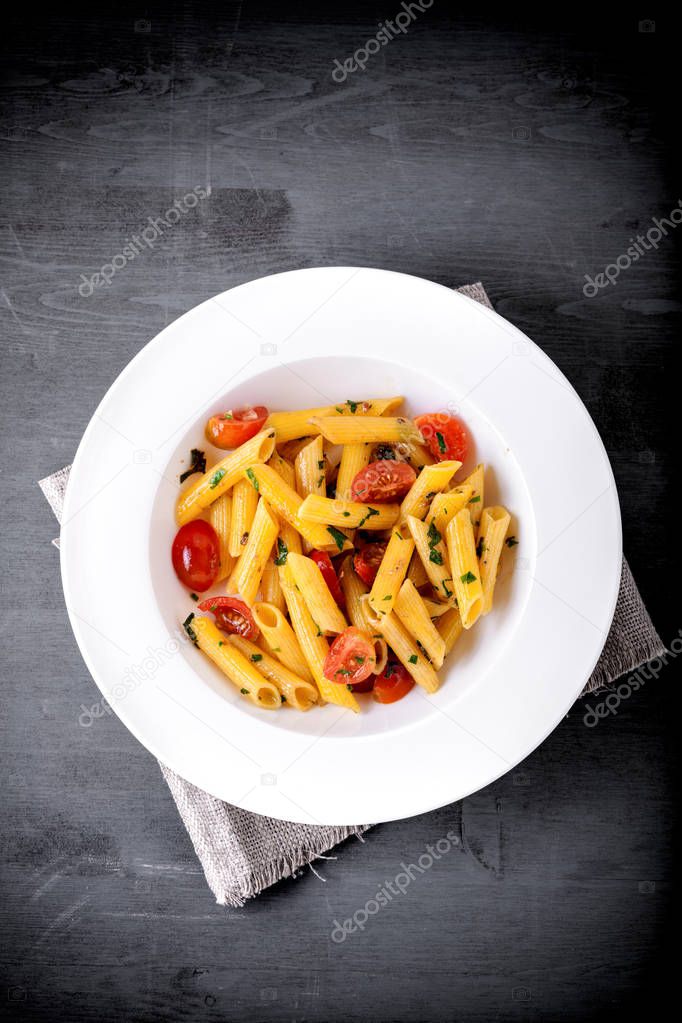 Penne with anchovy and tomato on a wooden surface.