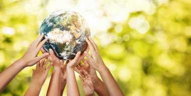 Group of children holding planet earth over defocused nature background with copy space clipart