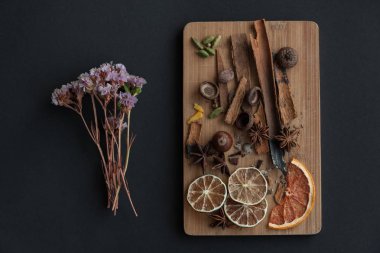Karışık baharat ve kuru narenciye dilimleri ile kesme tahtası. Üzerinde siyah arka plan ile sol tarafında kurutulmuş çiçek.
