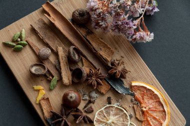 Kesme tahtası karışık baharat ile kuru narenciye dilimleri ile bazı siyah arka plan üzerinde sağ üst köşedeki çiçek kurumuş. Fotoğrafı kapatın