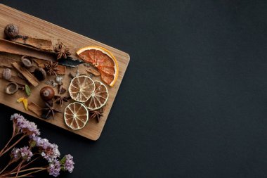 Karışık baharat ve kuru narenciye dilimleri ile kesme tahtası. Sol alt köşedeki kurutulmuş çiçek ile siyah arka plan üzerinde. Kopya alanı