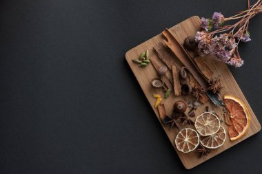 Karışık baharat ve kuru narenciye dilimleri ile kesme tahtası. Sağ üst köşedeki kurutulmuş çiçek ile siyah arka plan üzerinde. Kopya alanı