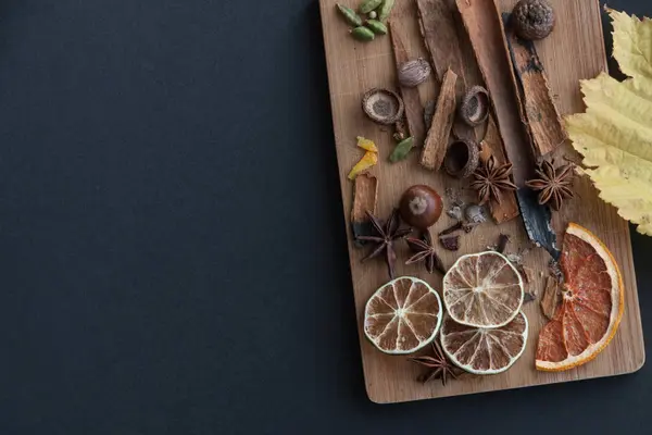 Karışık baharat ve kuru narenciye dilimleri ile kesme tahtası. Sağ tarafta bir sarı sonbahar yaprak siyah arka plan üzerinde. Uzay kopyalayın. Üstten Görünüm