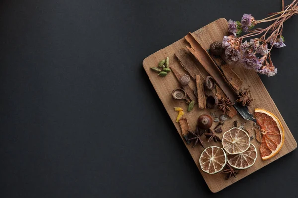 Karışık baharat ve kuru narenciye dilimleri ile kesme tahtası. Sağ üst köşedeki kurutulmuş çiçek ile siyah arka plan üzerinde. Kopya alanı
