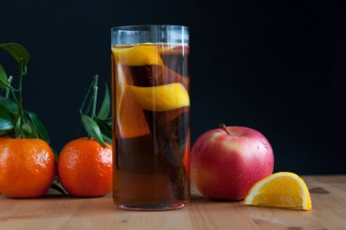 Bardak içki ısınma mevsimsel. Tarçın, limon kabuğu ve bazı meyve içinde. Ahşap masanın üstünde. Mandarine, elma ve portakal arka.