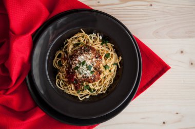 İtalyan bolognese ile köfte, domates sosu ve parmesan peyniri. İçinde karanlık plaka üzerinde kırmızı masa örtüsü ile ahşap masa.