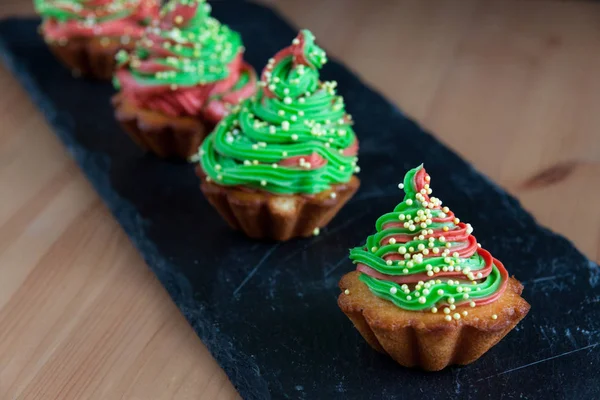 Рождественские кексы с зеленым и красным кремом на каменной тарелке, похожие на елку . — стоковое фото