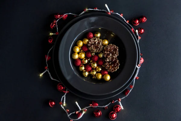 Decorações de Natal na placa preta no fundo escuro. Vermelho, bolas douradas e cones dentro e luz de Natal ao redor . — Fotografia de Stock