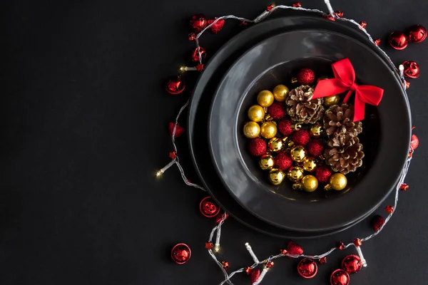 Decoraciones de Navidad en el plato negro en el fondo oscuro .Red, bolas de oro y conos en el interior y la luz de Navidad alrededor. —  Fotos de Stock