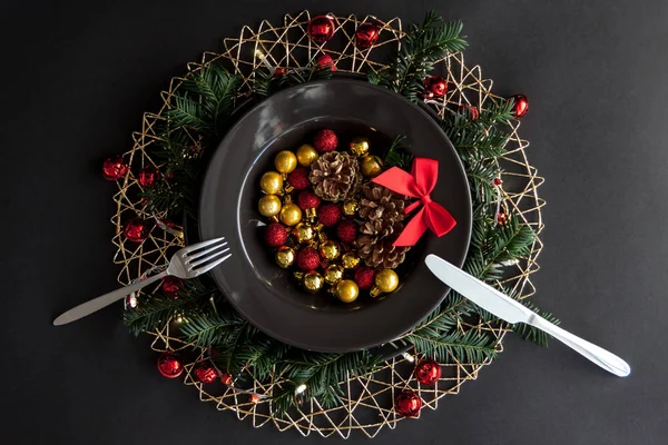 Decorazioni natalizie nel piatto nero con forchetta e coltello sullo sfondo scuro con alcuni ramoscelli di abete rosso. . — Foto Stock