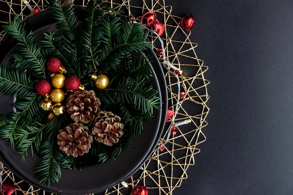 Décorations de Noël dans la plaque noire sur le fond sombre avec quelques brindilles d'épinette. Rouge, boules d'or et cônes à l'intérieur et lumière de Noël autour . — Photo