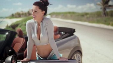 Karayipler kıyısında güzel, şık bir kadın çatısı olmayan bir arabanın yanında poz veriyor..