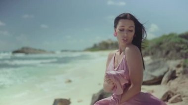 Deniz kıyısında, kameranın önünde poz veren pembe elbiseli güzel, şık bir kadın..