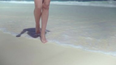 Güzel dişi bacakları beyaz kumda ve berrak deniz suyunda yürür..