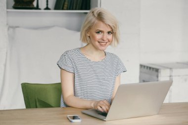 Güzel genç kız laptop önünde oturur. Onun yanında telefon