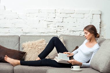 Kanepede kitap okuyan kadın.