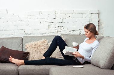 Kanepede kitap okuyan kadın.