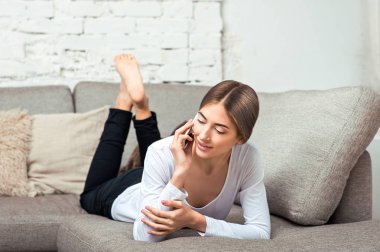 Kadın kanepede yatan cep telefonuyla söz