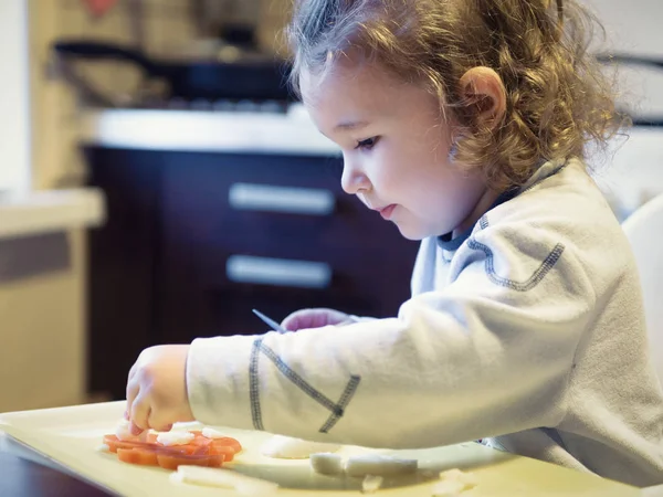Двухлетний ребенок режет морковь и картошку на кухне — стоковое фото