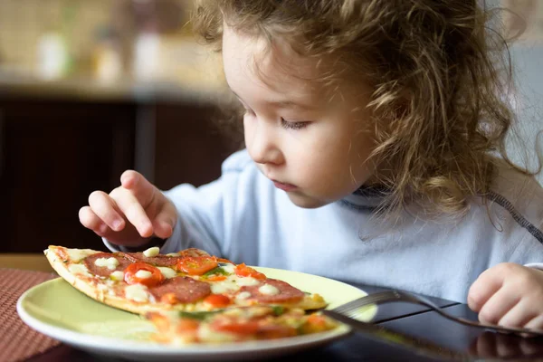 Child looks at pizza on table. Three years old kid is going to e