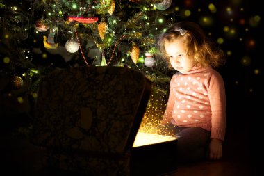 Noel ağacının yanındaki çocuk sihirli sandığı açıyor. Çocuk içine bakıyor.