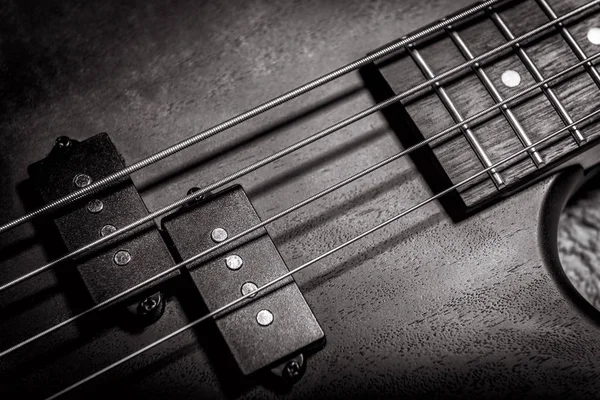 Bass guitar with four strings in black and white closeup. Detail