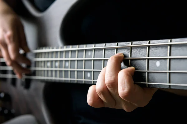 Bass guitar player hand closeup, lesson and practice theme. Playing on bass electric guitar, live music and skill concept. Close view of guitarist fingers on bass fretboard.